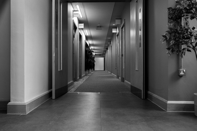 A corridor seen from a tiled floor, clean and empty, doors closed along its length.
