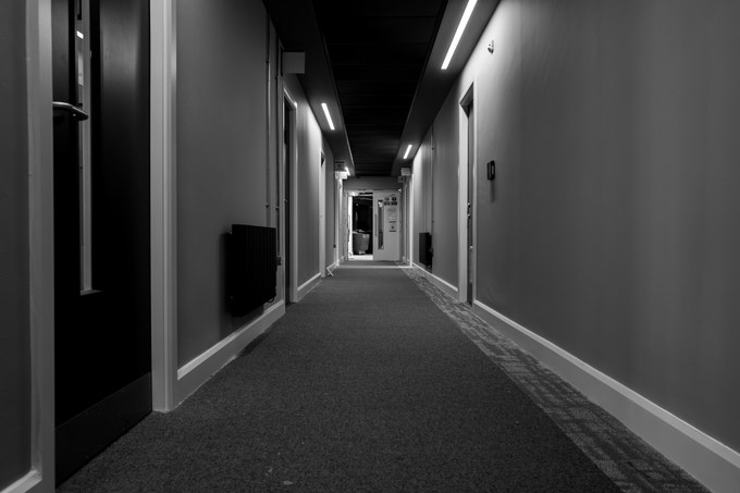 A radiator on the wall of an empty corridor, lights running, a lit doorway at the end.