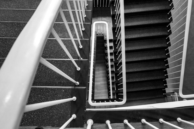 A stairwell photographed from above, white handrails turning down through the floors.