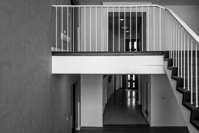 A stair landing and balustrade, a lit corridor visible through the opening beyond.