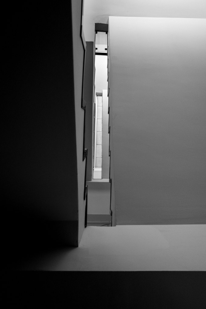 A stairwell void looking up, a tall narrow shaft of light between blank walls.