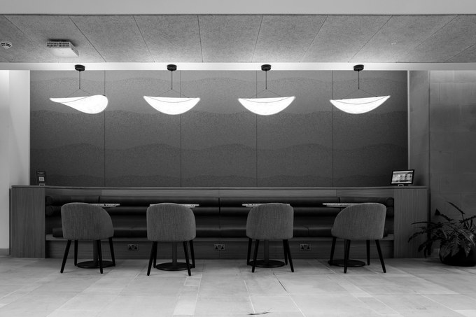 Four chairs squared to a bench desk beneath four pendant lights, a screen switched on, nobody there.