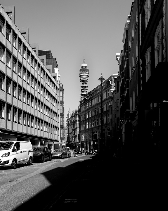 A Fitzrovia street in hard morning light, a 1960s office block along one side and the BT Tower closing the view at the far end.