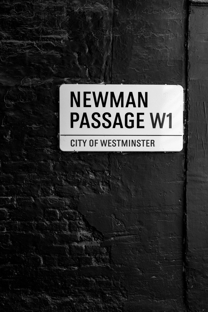 A City of Westminster street sign reading Newman Passage W1, fixed to a wall of black-painted brick.