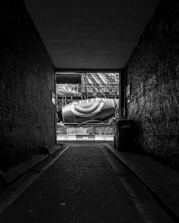 Looking out from the covered section of Newman Passage to a cement mixer and construction hoarding in the daylight beyond.