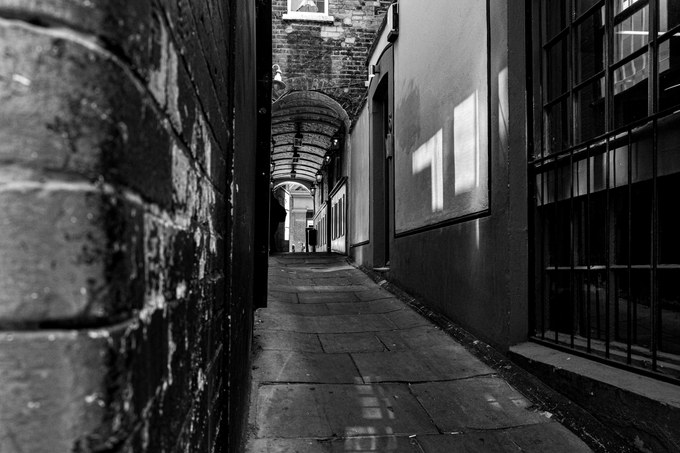 A narrow London passage running under a brick barrel vault, flagstones below and patches of reflected light on the wall.