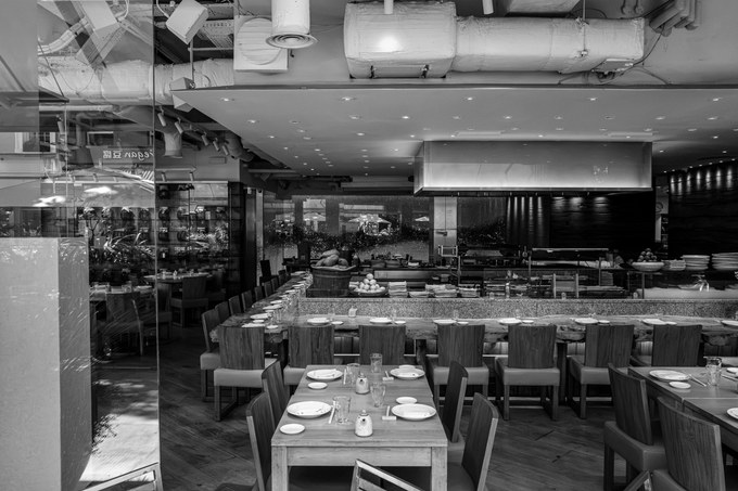 The interior of ROKA on Charlotte Street seen through plate glass, tables laid and empty, the robata grill and kitchen pass beyond.