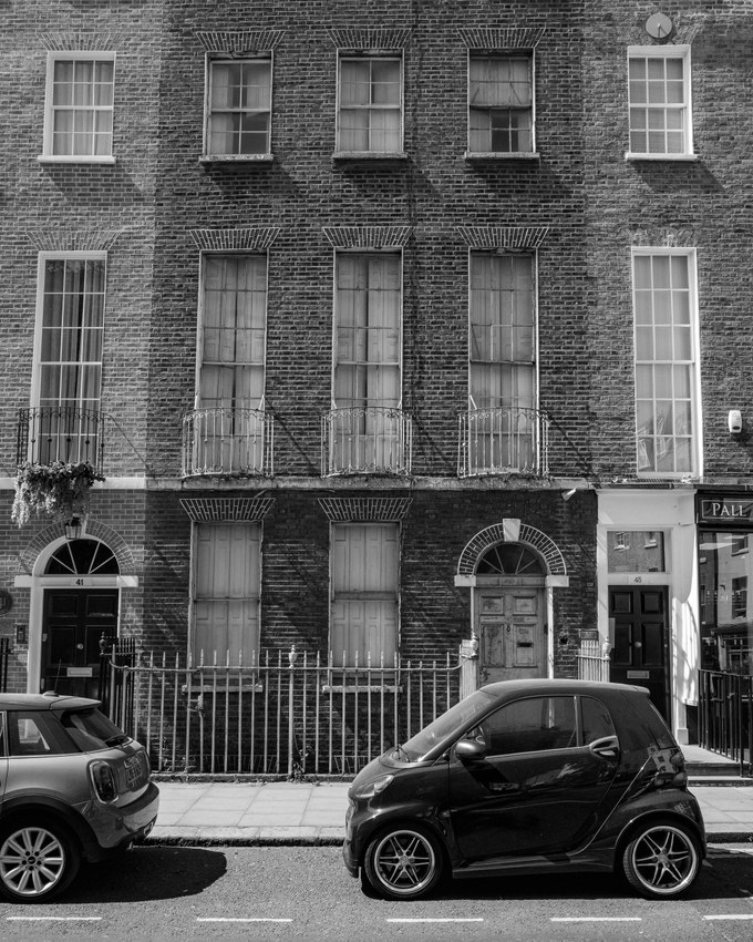 A Georgian brick terrace photographed square-on, sash windows and shuttered ground floor, two small cars parked at the kerb.