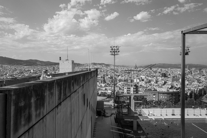 The diving boards and a concrete wall at the pool's edge, the city and the hills beyond under a sky of broken cloud.