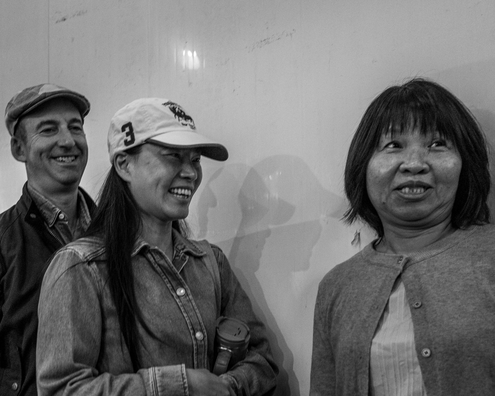 Three people standing against a white wall in Kirkgate Market, all laughing at something out of frame.