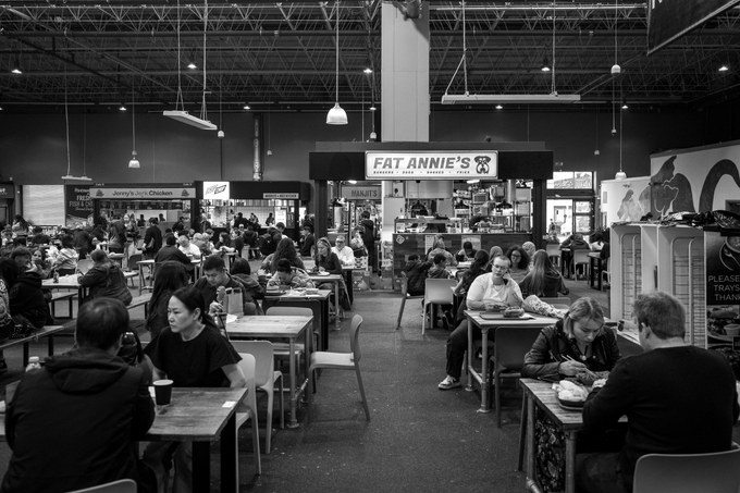 A busy market food hall, people eating at long tables beneath a Fat Annie's sign.