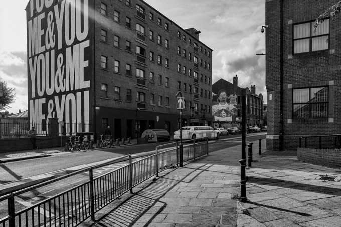 A brick block painted with the words Me and You, You and Me, a sunlit pavement and railings in front.
