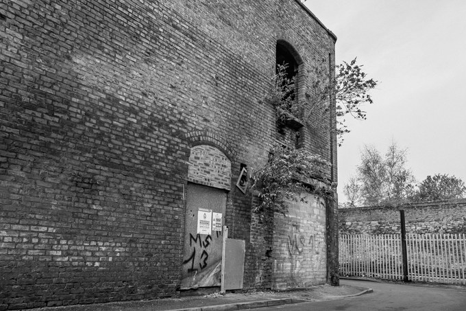 A blocked arched doorway in the brick side wall of the New Osborne, down a fenced alley.