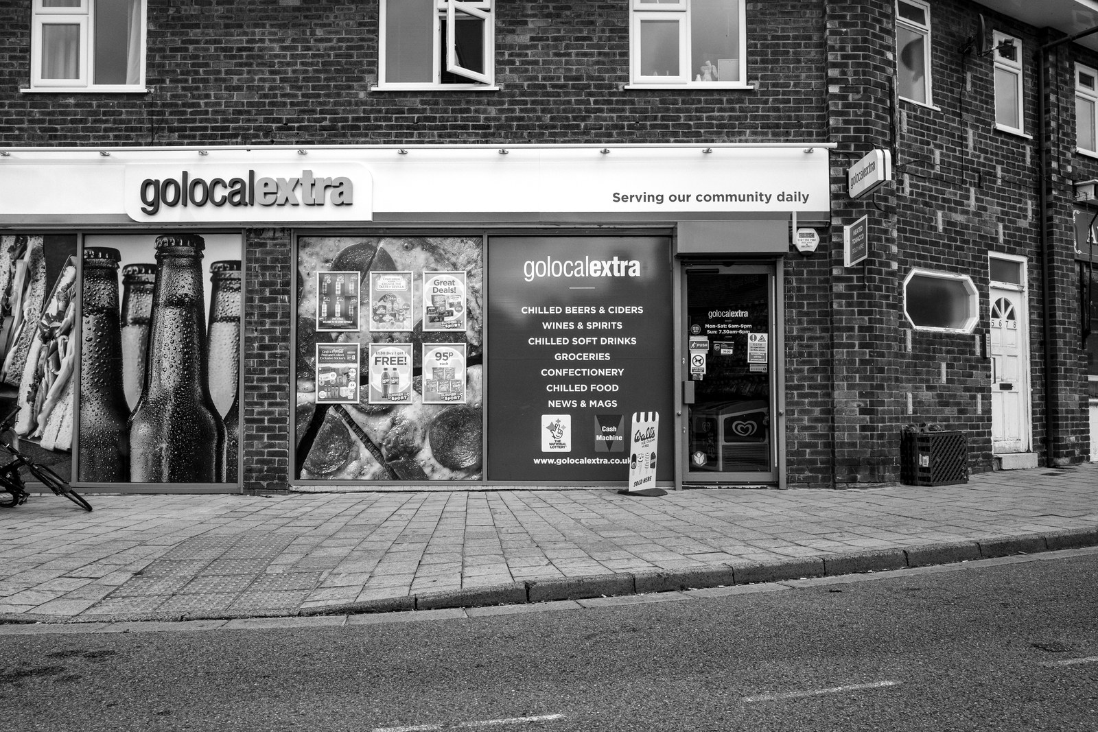 A mini market on Chapel Lane, Wilmslow, its golocalextra fascia above a window of advertising boards, the pavement empty.