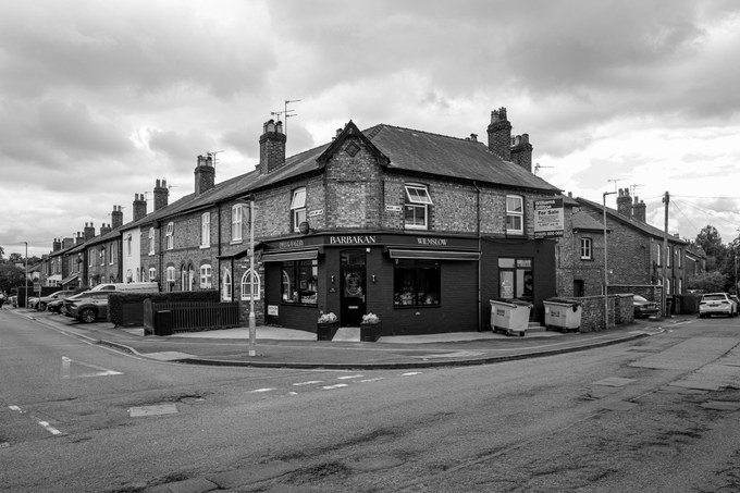 The Barbakan delicatessen on the corner at Wilmslow, a dark shopfront set into a brick terrace under a heavy sky.